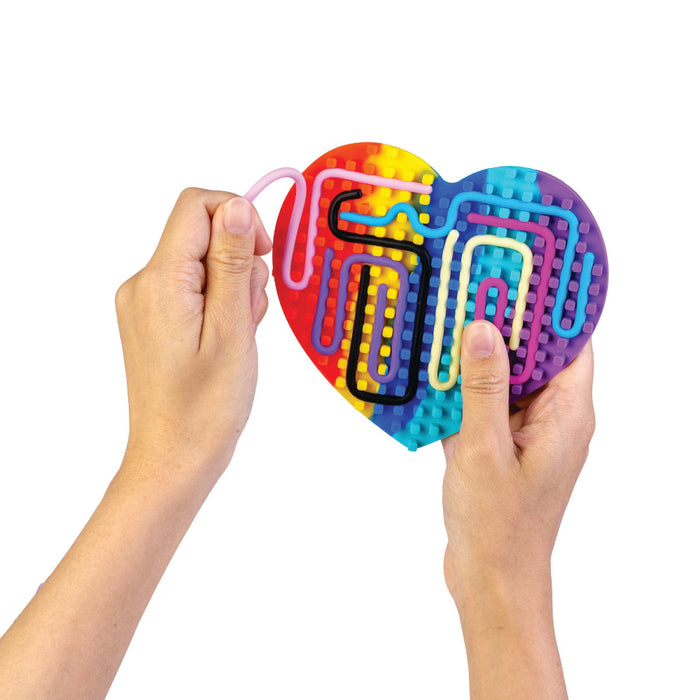 Heart-shaped maze toy with colorful pathways held by hands on a white background